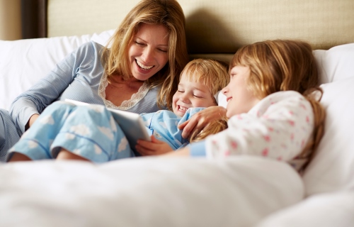 Mutter mit 2 Kindern beim Lesen im Bett